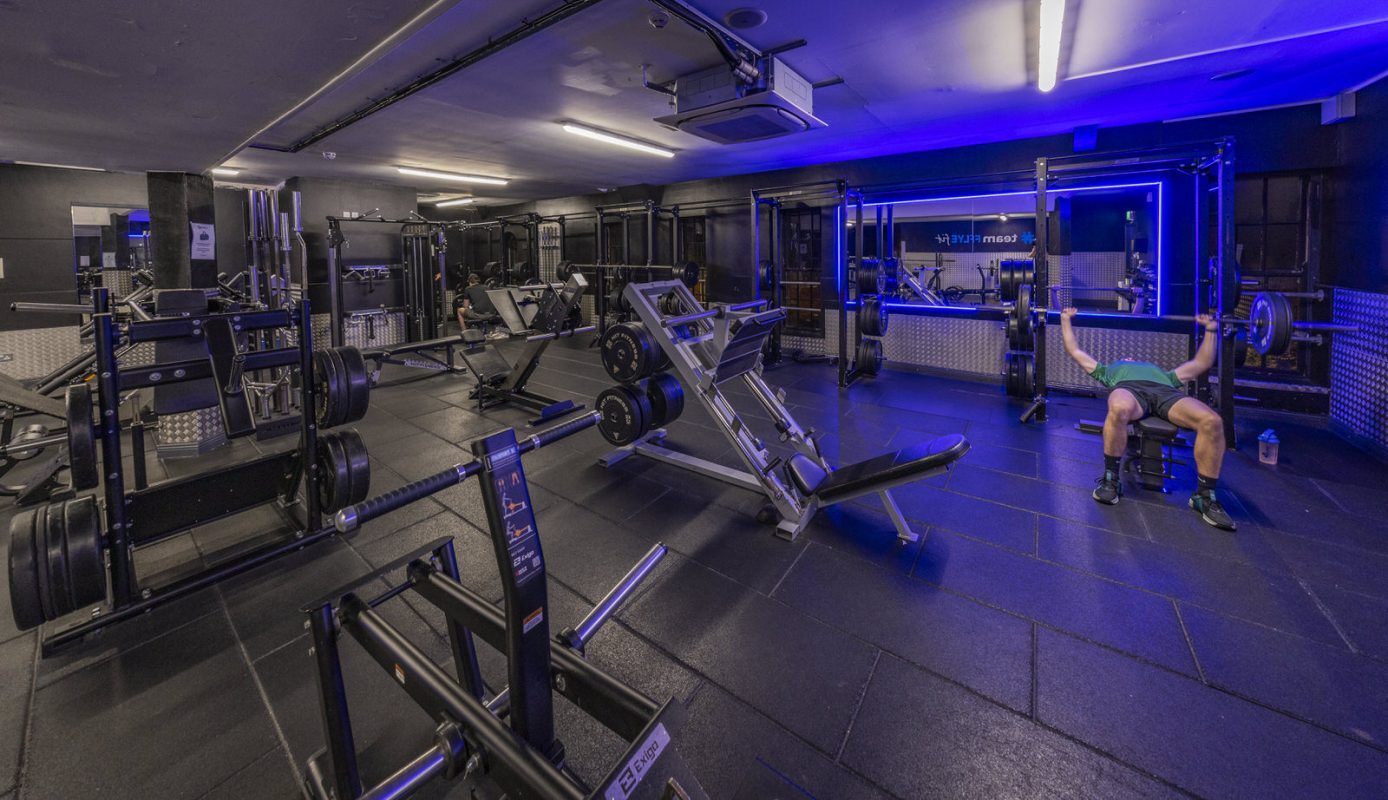 FLYEfit Ranelagh gym floor with free weights and strength equipment under blue lighting, Dublin 6 — near EirStay corporate apartments
