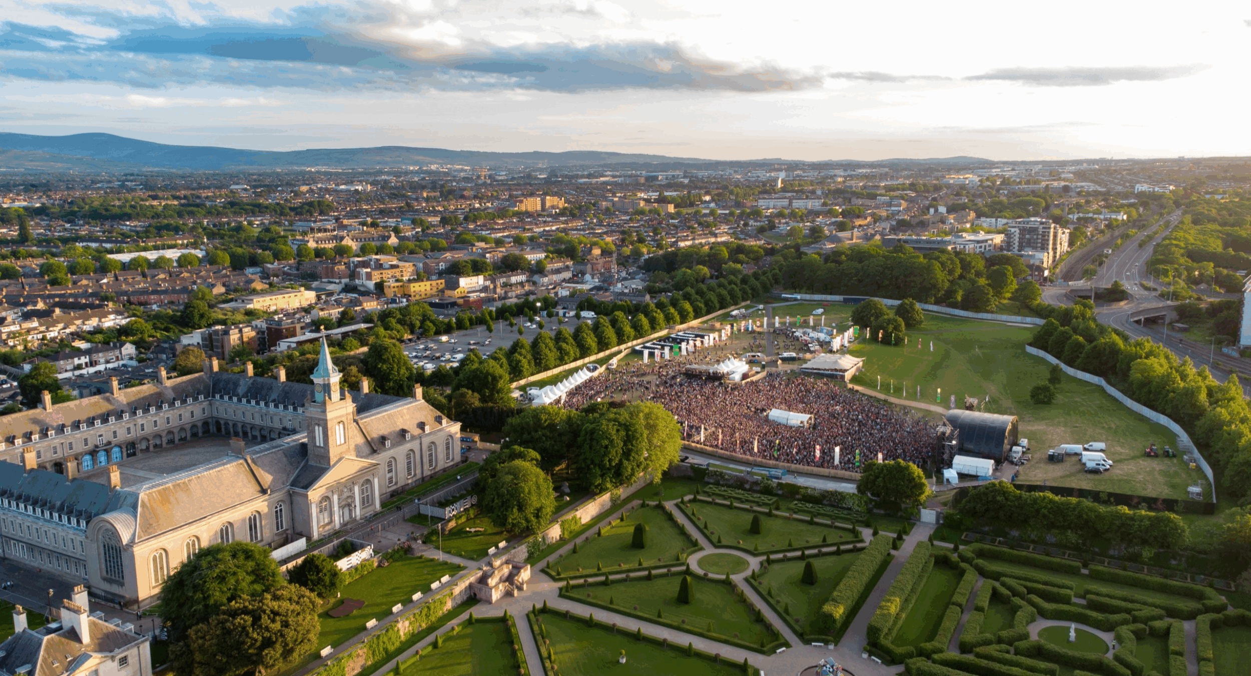 Aerial view of IMMA — the Irish Museum of Modern Art at the Royal Hospital Kilmainham, Dublin 8 — with Forbidden Fruit festival crowd filling the grounds and formal parterre gardens in the foreground, walkable from EirStay serviced accommodation in Kilmainham and Sandford Gardens