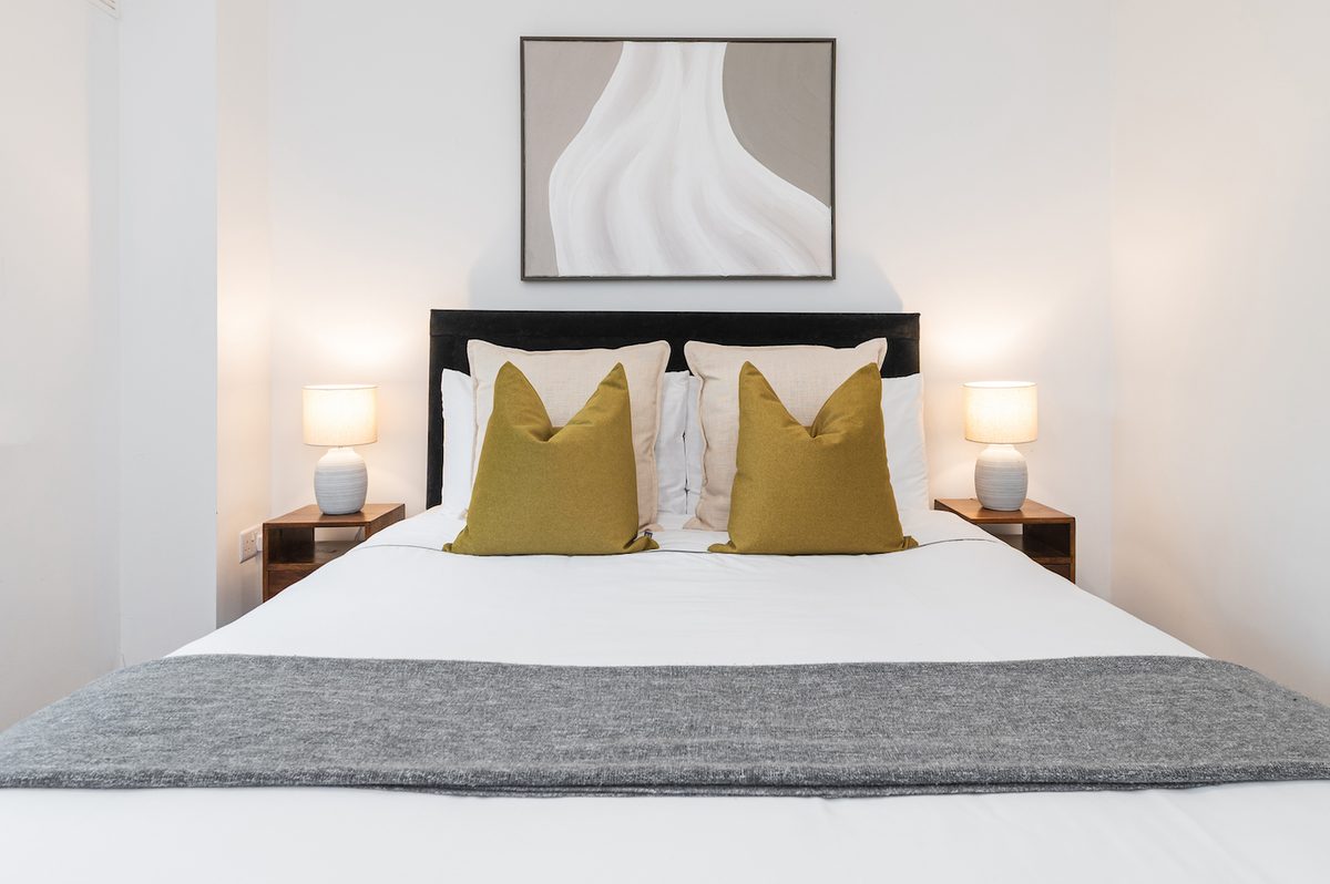 Double bedroom with grey throw, twin bedside lamps and framed art in EirStay Islandbridge one-bedroom serviced apartment Dublin 8