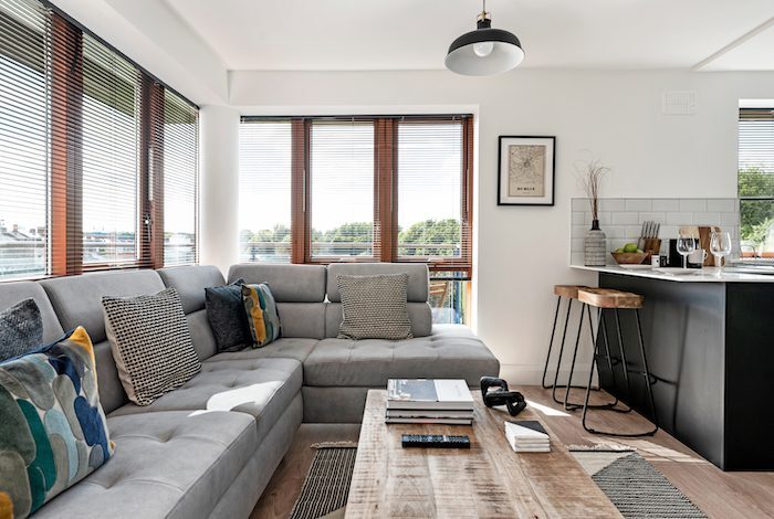 Grey corner sofa with colourful cushions and wooden coffee table facing kitchen breakfast bar in EirStay corporate accommodation Kilmainham Dublin 8