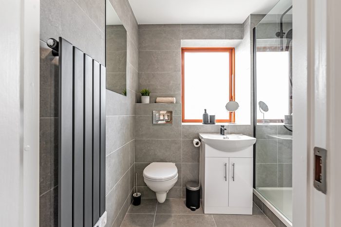 Modern bathroom with grey tiles vertical radiator wall-hung toilet and walk-in shower in EirStay corporate short stay Kilmainham Dublin 8