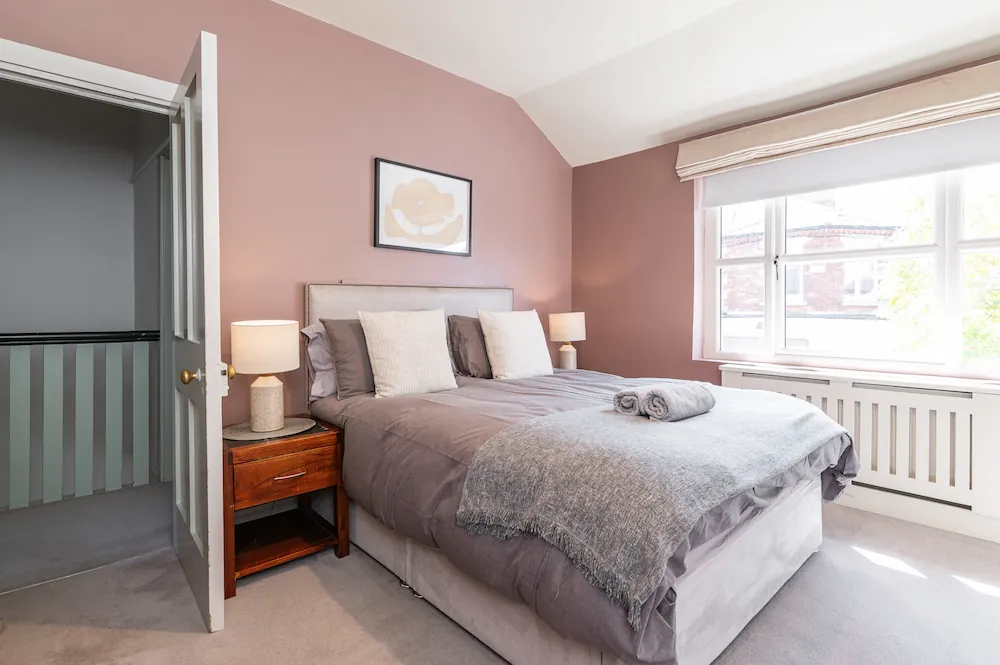 Double bed beside a large window in a pink bedroom at Sandford Gardens