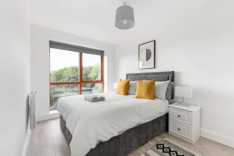 King-size bedroom with mustard cushions Hilma af Klint print and floor-to-ceiling window with tree views in EirStay corporate accommodation Kilmainham Dublin 8