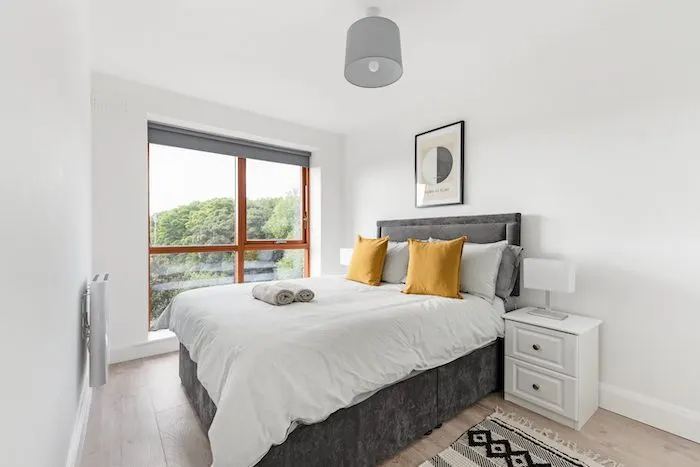 King-size bedroom with mustard cushions Hilma af Klint print and floor-to-ceiling window with tree views in EirStay corporate accommodation Kilmainham Dublin 8
