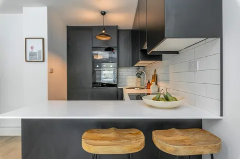 White breakfast bar with wooden stools, integrated oven and extractor in EirStay Islandbridge serviced apartment kitchen Dublin 8
