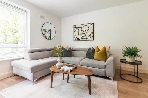 Light-filled living room with corner sofa, round mirror and house plants in EirStay Islandbridge one-bedroom apartment Dublin 8