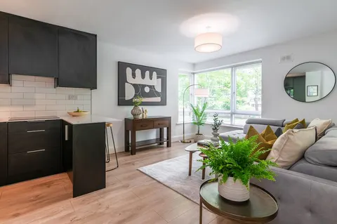 Open-plan living and kitchen area in EirStay Islandbridge serviced apartment Dublin 8 — matte-black fitted kitchen with breakfast bar and bright corner-sofa lounge