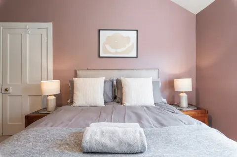 Double bed with grey bedding, bedside lamps and framed artwork in the first bedroom at Sandford Gardens