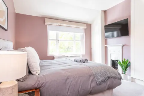 First bedroom with a double bed and wall-mounted television above the fireplace at Sandford Gardens