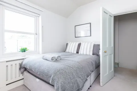 Second bedroom with a double bed, striped pillows and a bright window at Sandford Gardens
