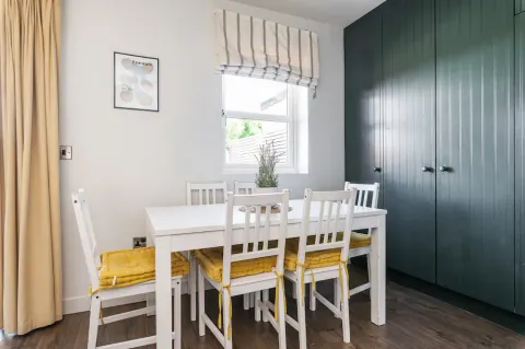 Dining table and chairs beside a window and dark green cabinetry at Sandford Gardens